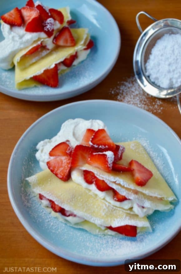 Strawberry Dream Crêpes 3 Close-up of Strawberry Cream Cheese Crêpes on pale blue plates, showcasing the fresh strawberries, creamy filling, and powdered sugar dusting.