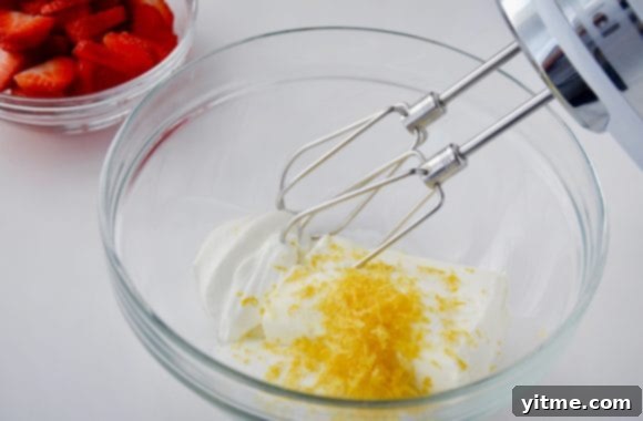 Strawberry Dream Crêpes 5 Image of a glass bowl with cream cheese, sour cream, sugar, and lemon zest, along with a handheld beater and fresh strawberries.