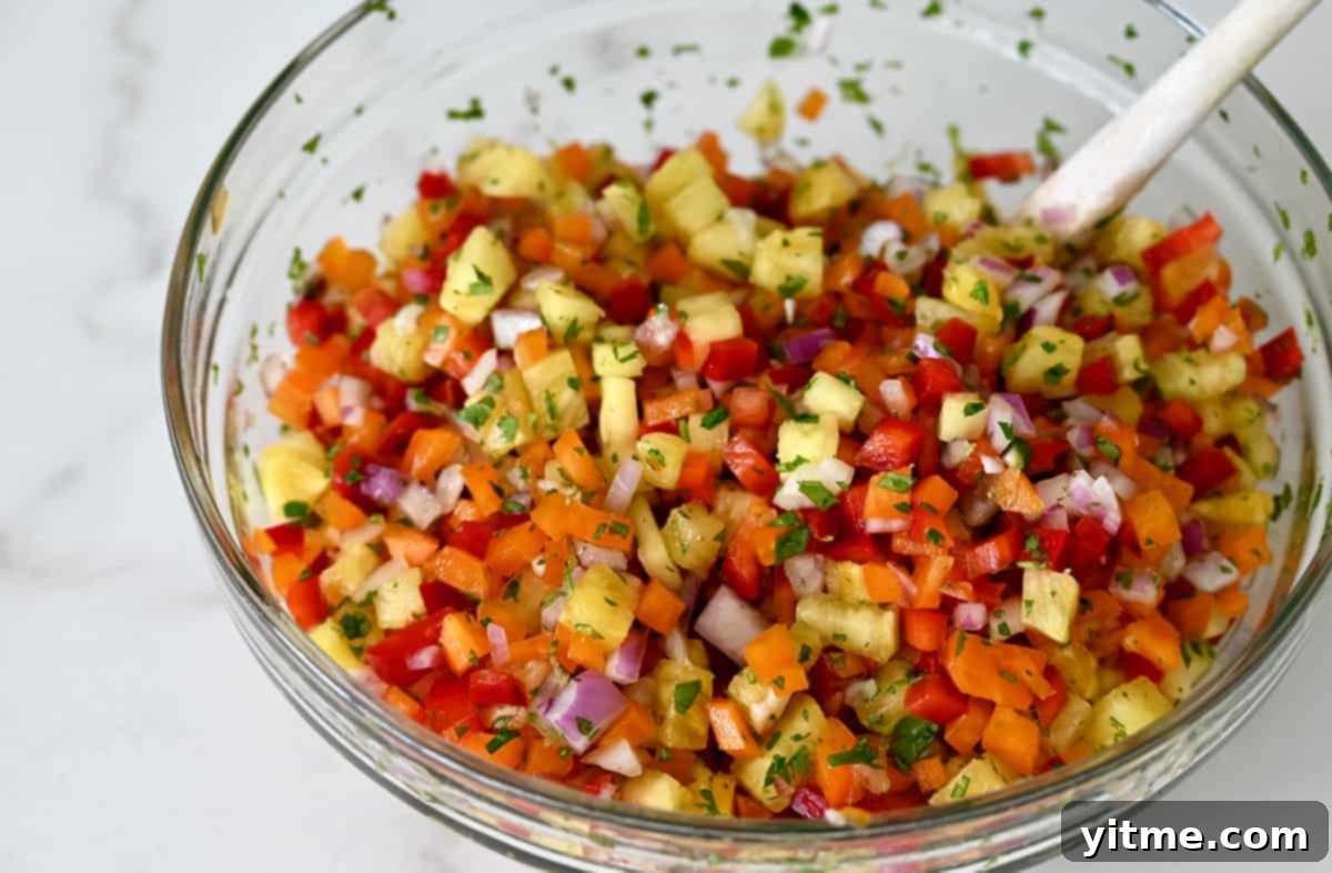 A clear bowl with a spoon, filled with pineapple salsa featuring bell peppers and fresh cilantro, ready to be served.