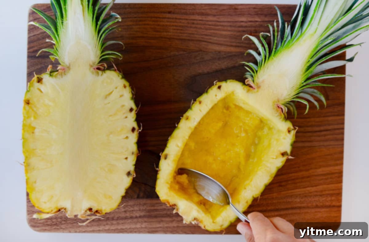 A beautifully hollowed-out pineapple bowl placed next to its other half on a wooden cutting board.