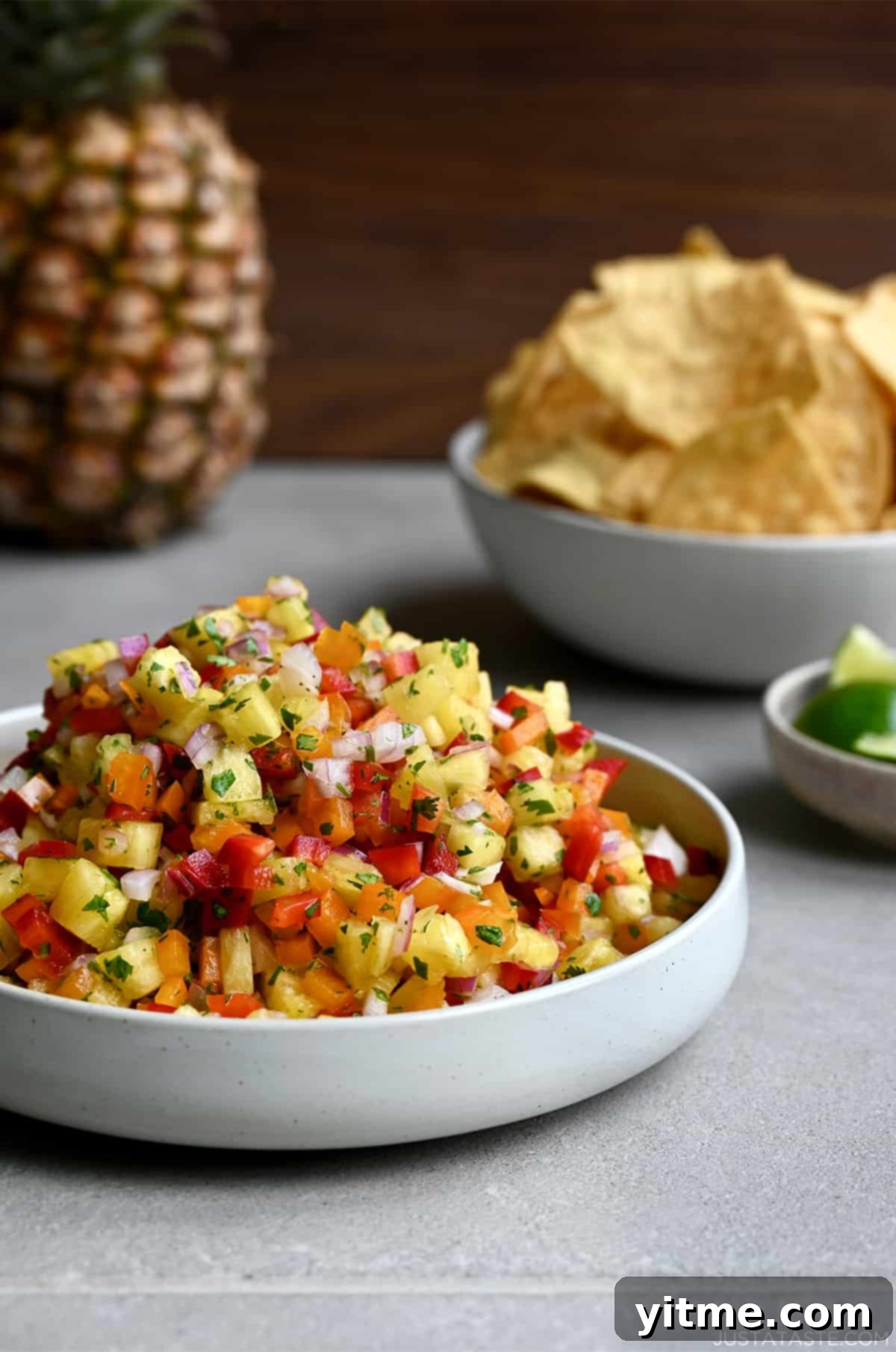 A white bowl brimming with fresh pineapple salsa, accompanied by a smaller bowl filled with crispy tortilla chips, perfect for dipping.
