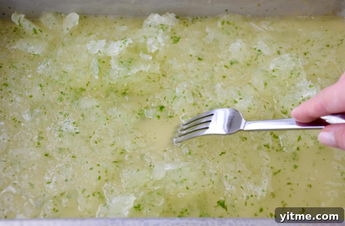 A fork scrapes partially frozen granita on a baking sheet.