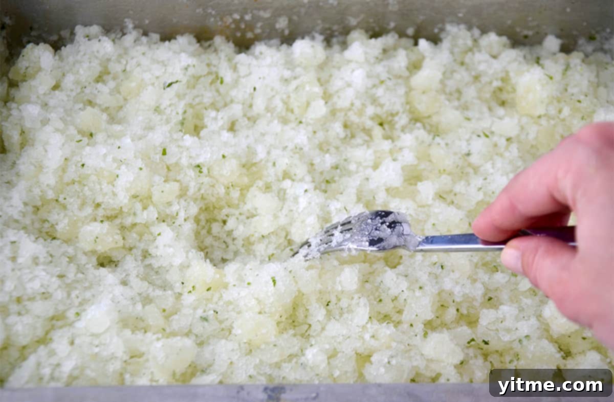 A hand holding a fork stirs frozen lemonade on a baking sheet.