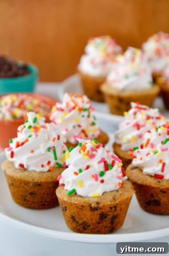 Muffin Tin Chocolate Chip Cookie Treats 2 A white plate containing Chocolate Chip Cookie Cups topped with frosting and rainbow sprinkles