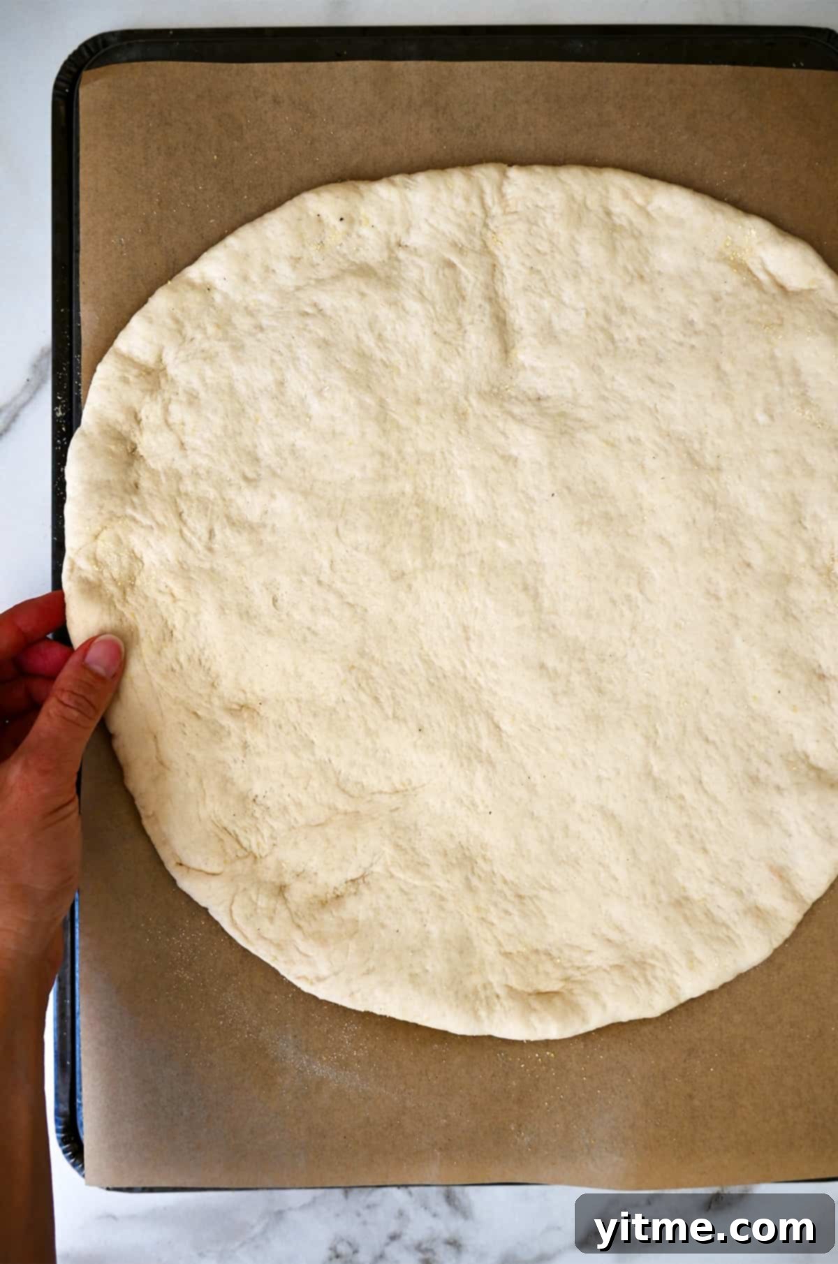 Freshly rolled pizza dough, perfectly circular, sits on a parchment paper-lined baking sheet, ready for toppings.