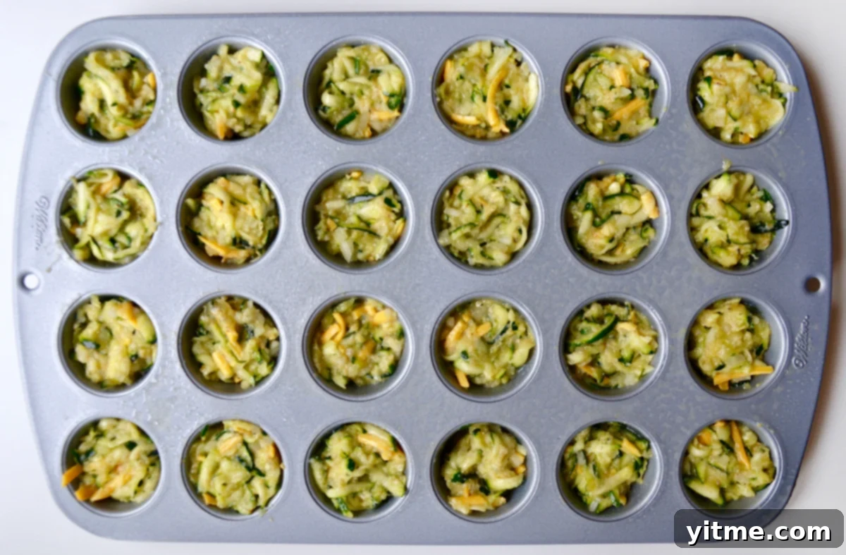 A mini muffin pan containing zucchini tot batter.