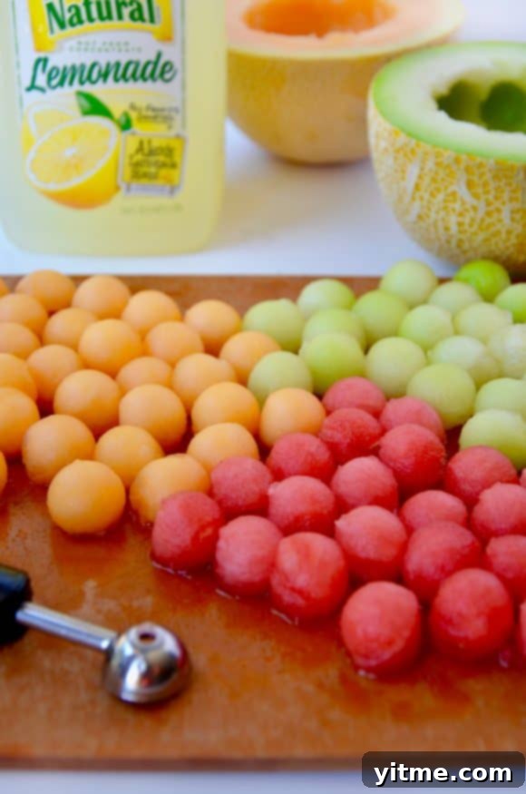 Melon balls on a cutting board with lemonade in the background