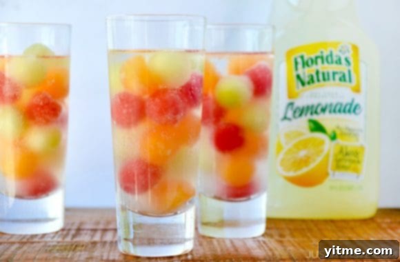 Three clear cocktail glasses containing melon balls with a jug of lemonade