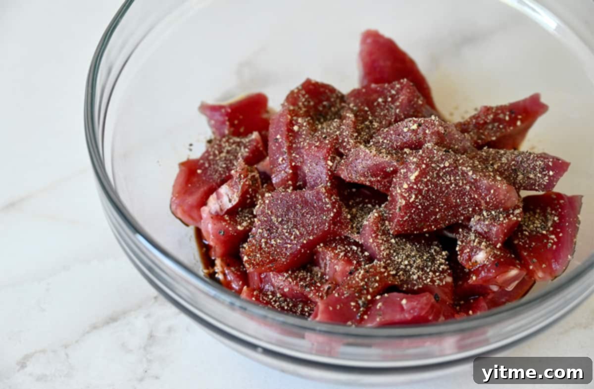 Pork tenderloin pieces in a black pepper marinade in a glass bowl.