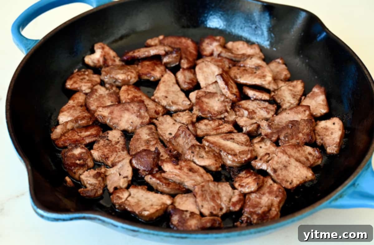 Browned pork pieces sizzling in a large skillet, cooking evenly.