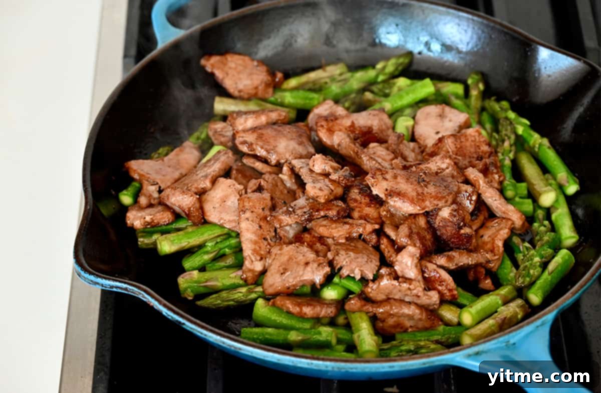 Stir-fried black pepper pork and crisp-tender asparagus pieces in a large skillet, ready to serve.