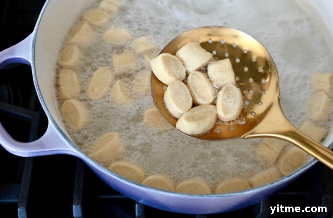 A top-down view of a slotted spoon with dough over a pot containing baking soda and water