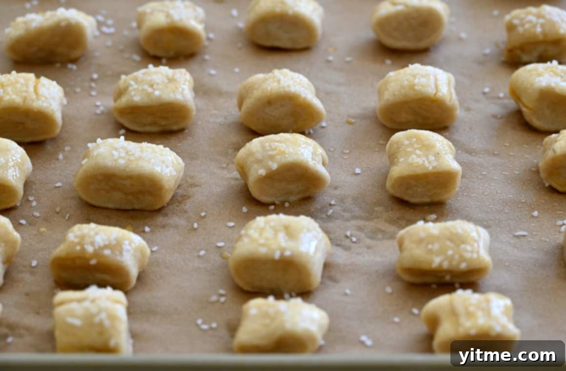 Unbaked soft pretzel bites topped with egg wash and sea salt on a parchment paper-lined baking sheet