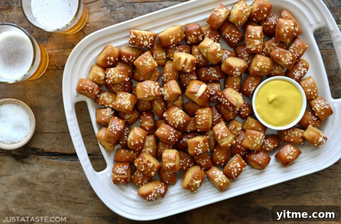 Glasses of beer next to a serving platter containing the best homemade soft pretzel bites and a small ramekin filled with yellow mustard
