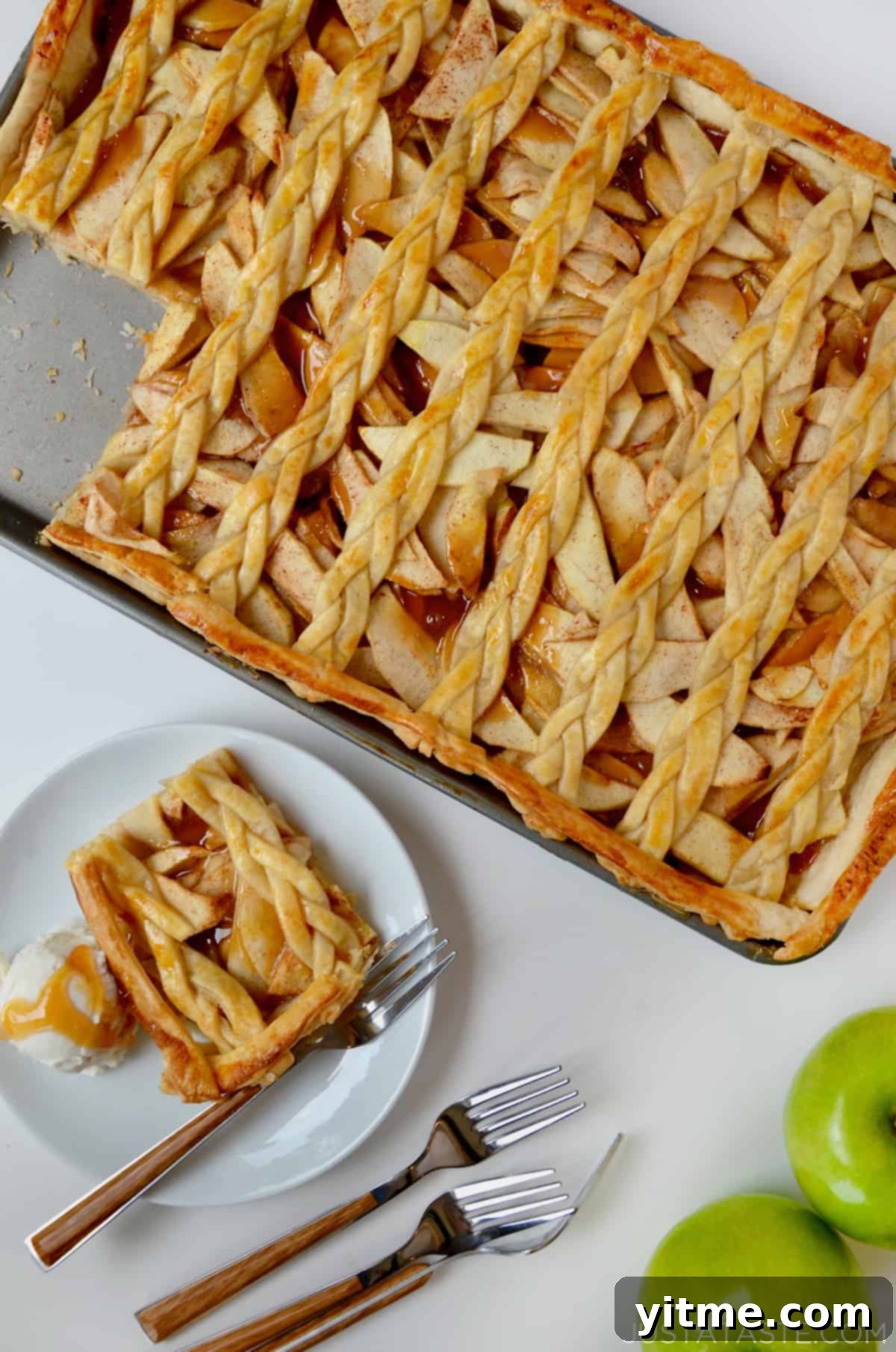 A sheet pan with caramel apple slab pie with a lattice topping next to a plate with a slice of pie and a scoop of vanilla ice cream.