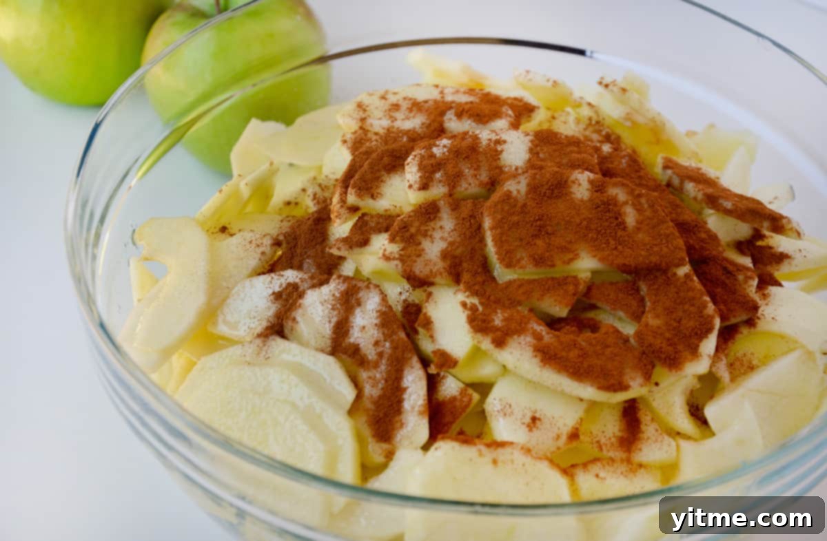 A medium glass bowl with apples, sugar, cornstarch, cinnamon and lemon juice.