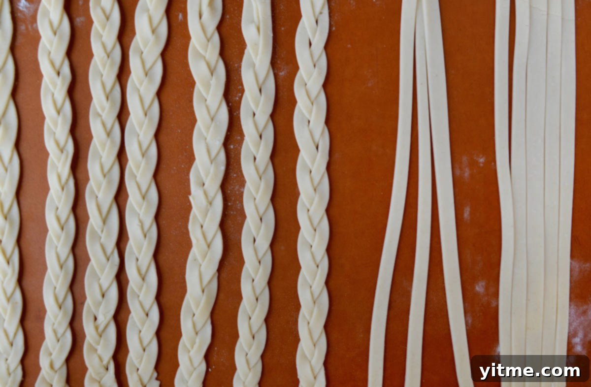 A cutting board with pie dough that has been cut into three long 1/2-inch strips and pie dough that has been braided into five braids for the lattice top.