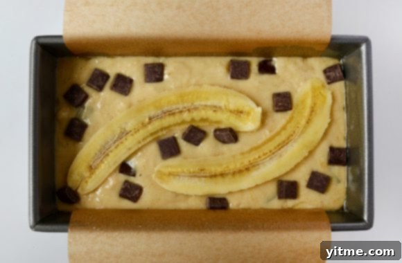 Sour Cream Chocolate Chunk Banana Bread batter in pan, topped with chocolate chunks and sliced banana