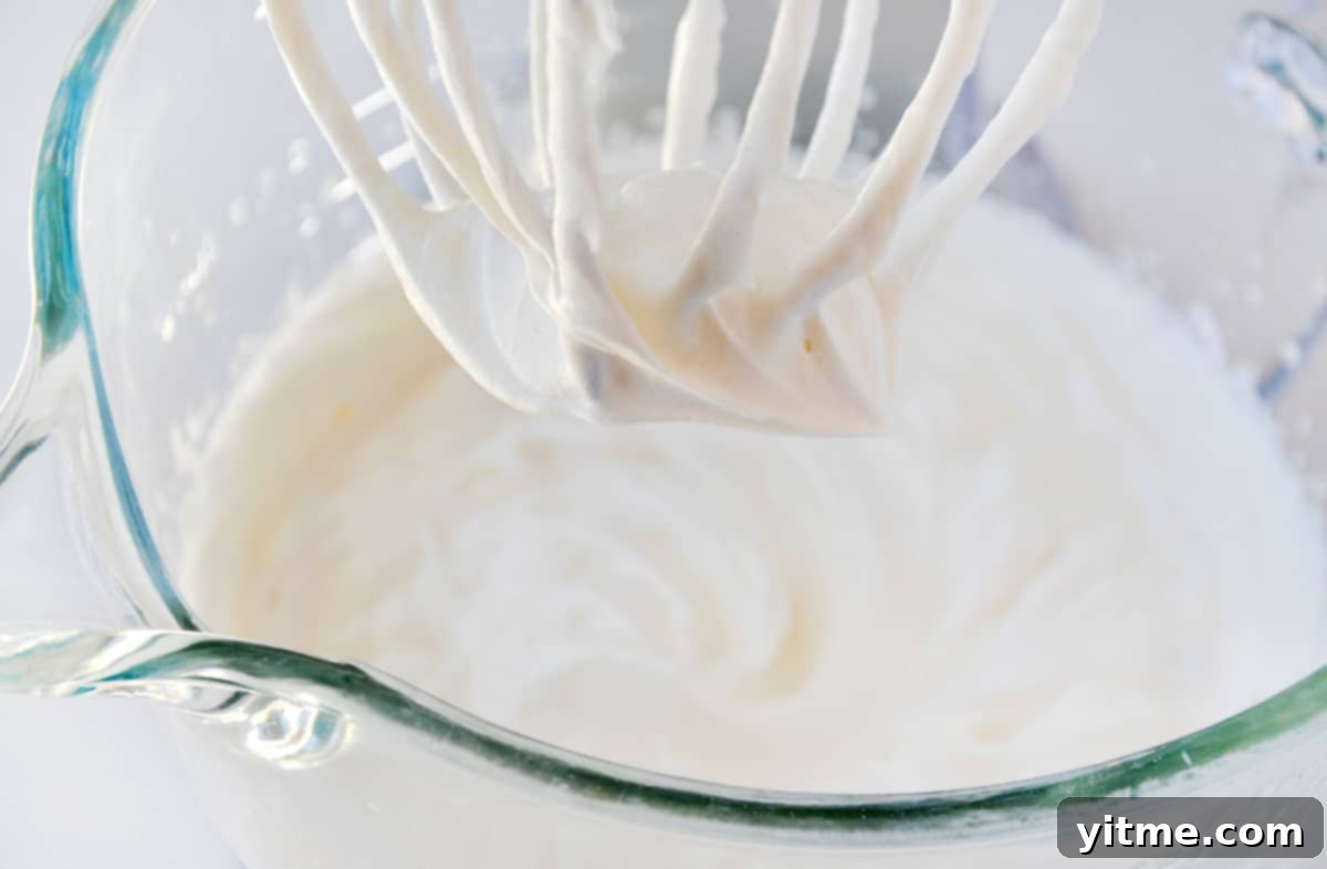 Whipped cream in the bowl of a stand mixer fitted with the whisk attachment.