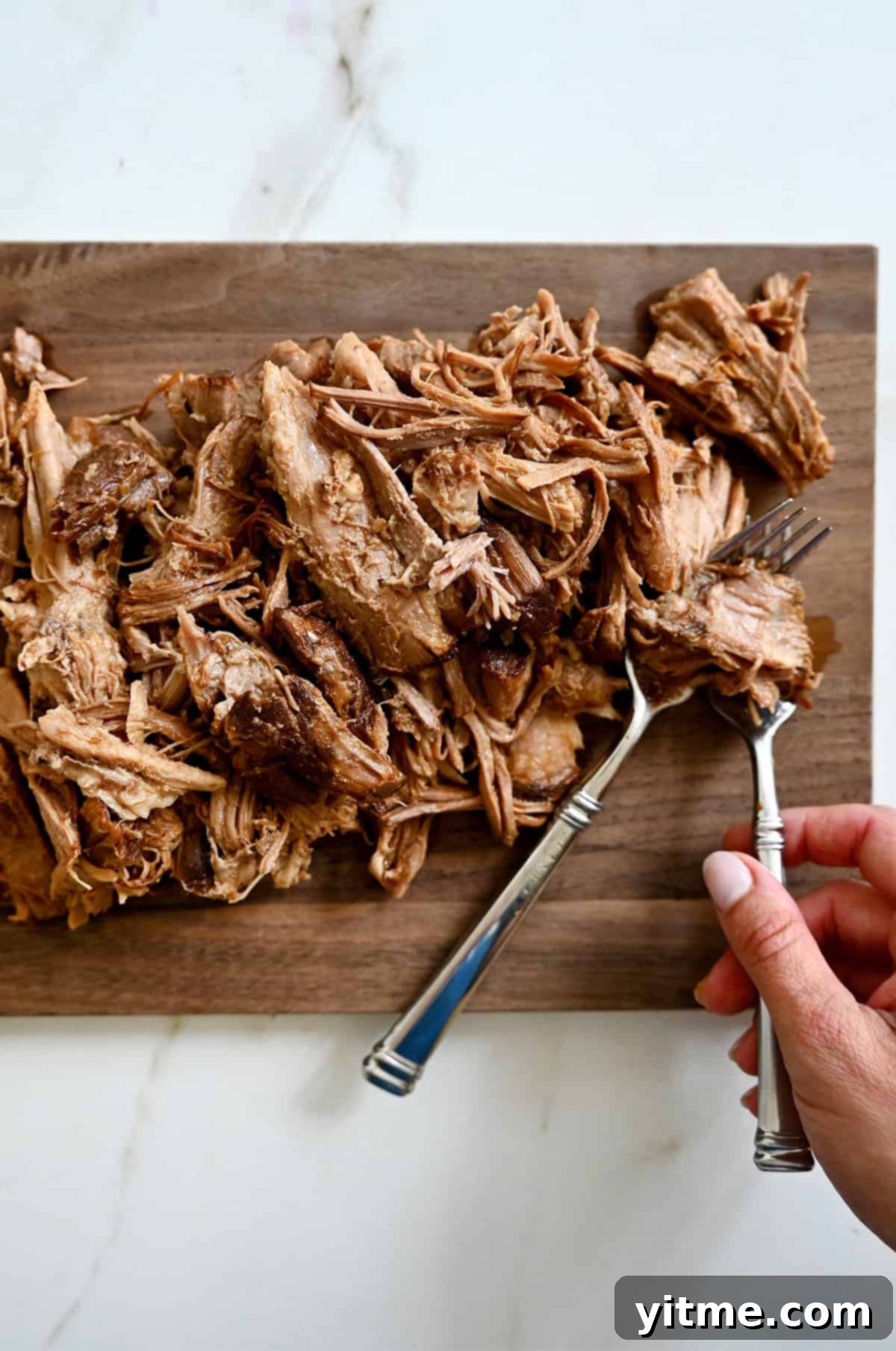 Using two forks to shred slow-cooked pork on a cutting board