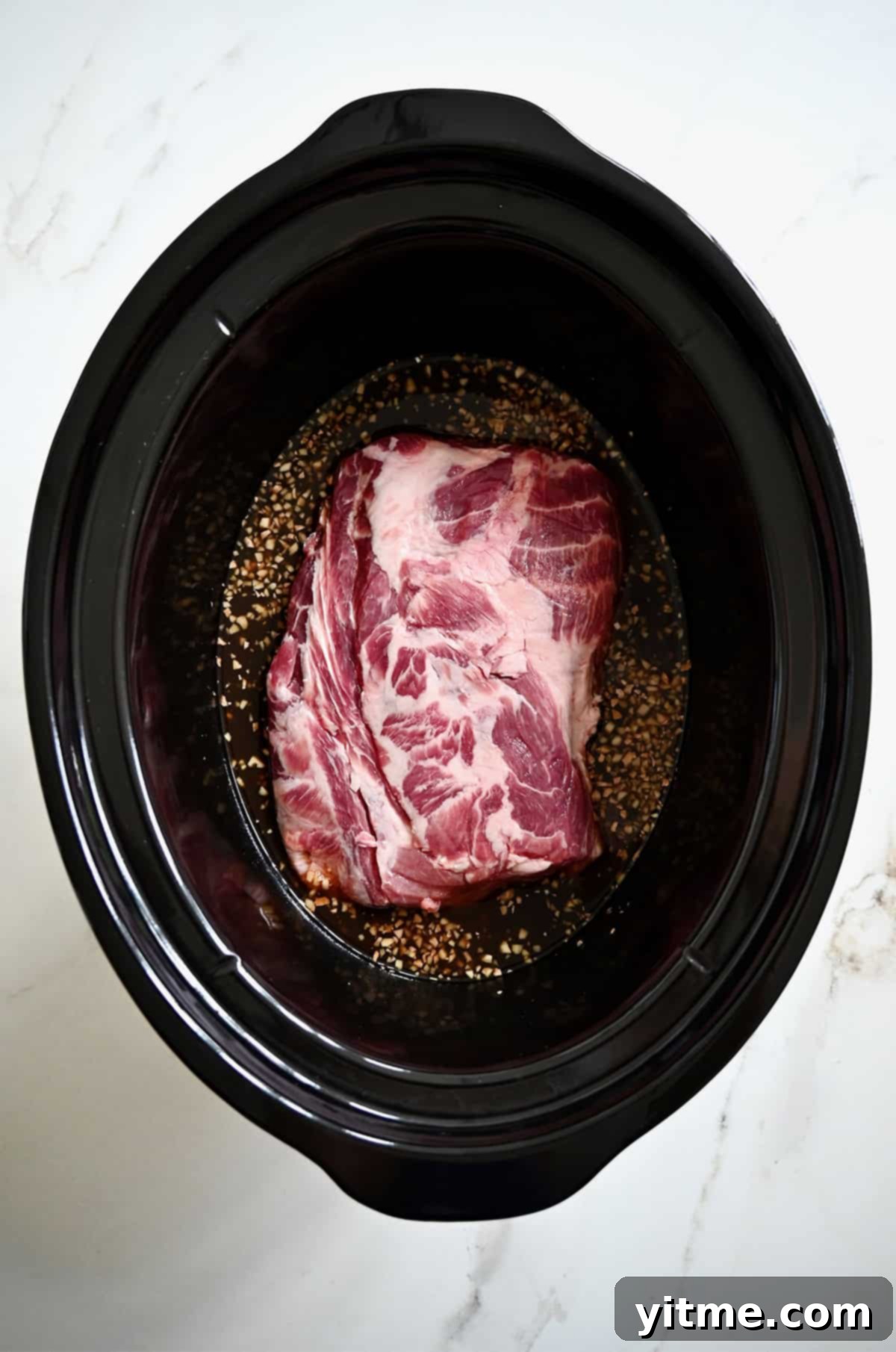 A pork butt in a slow cooker with a homemade sweet and tangy sauce