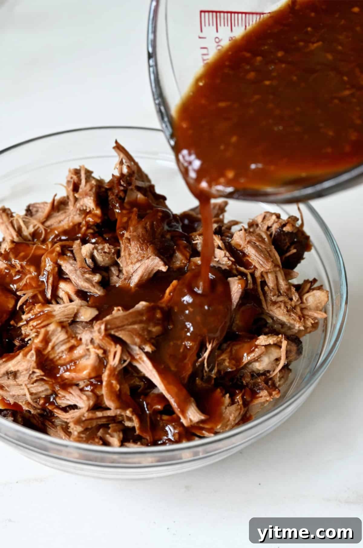 Pouring a sticky pineapple soy sauce over pulled pork in a bowl