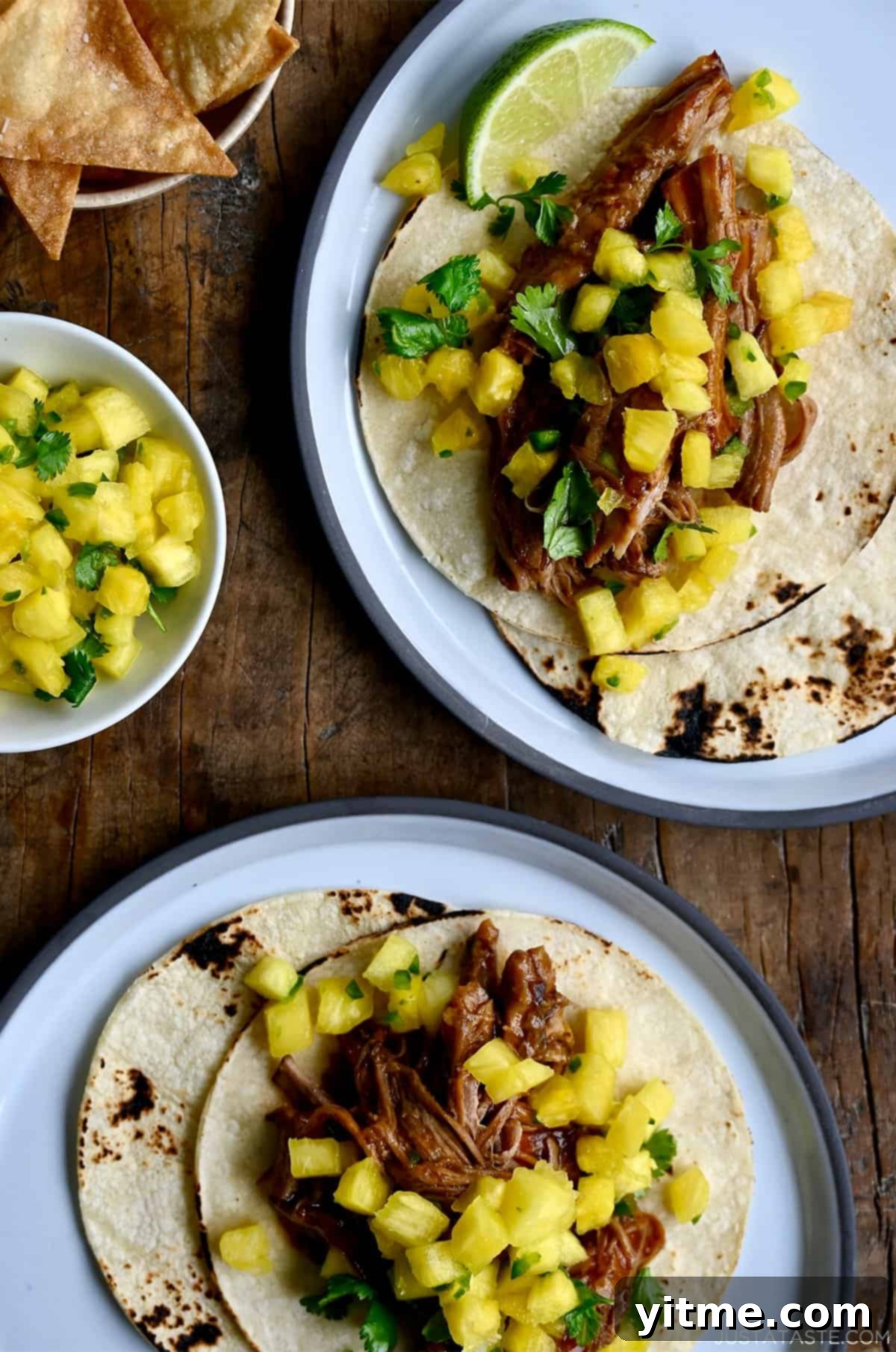 Hawaiian pulled pork tacos with fresh pineapple chunks and cilantro near a bowl with homemade tortilla chips