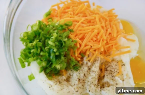 Bowl of leftover mashed potatoes, chopped scallions, shredded cheddar cheese, and eggs ready to be mixed
