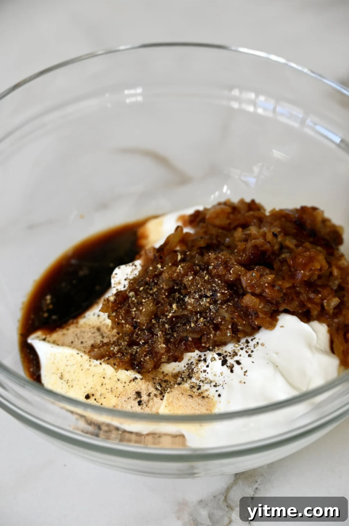 Elevated Homemade French Onion Dip 5 Mixing ingredients for French onion dip in a glass bowl.