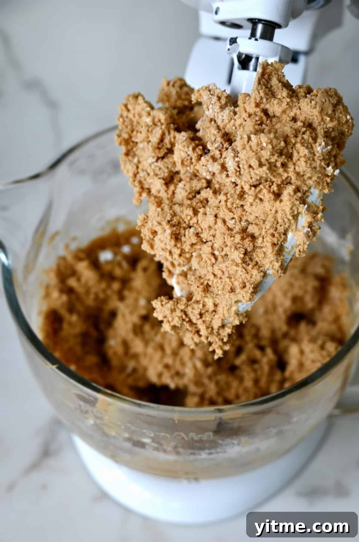 A stand mixer with a peanut butter and graham cracker crumb mixture on the paddle attachment.