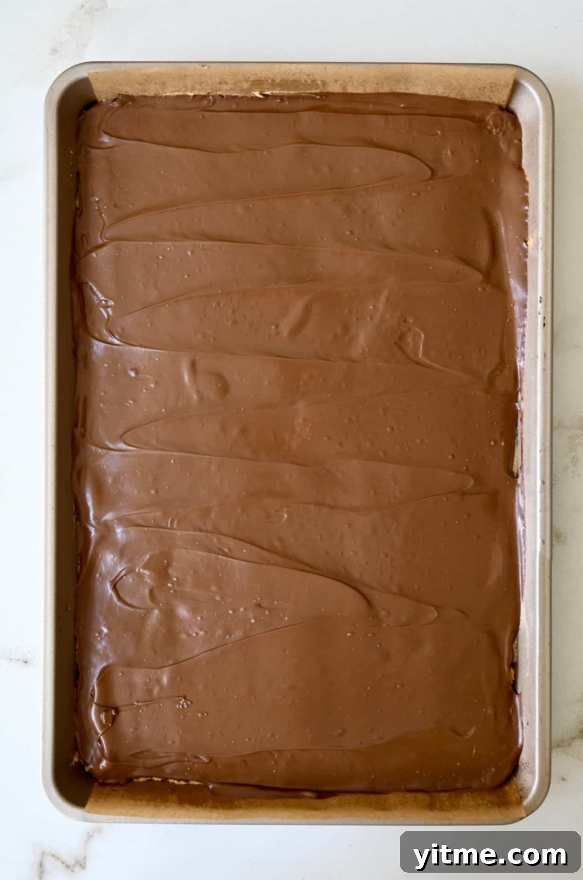 Melted chocolate spread over peanut butter bars in a baking pan.