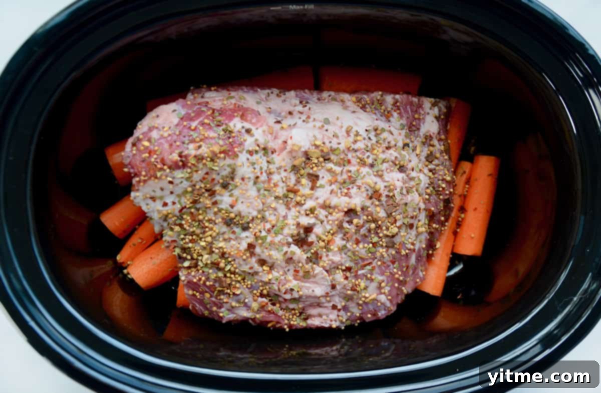Corned beef on a bed of carrots in a slow cooker.