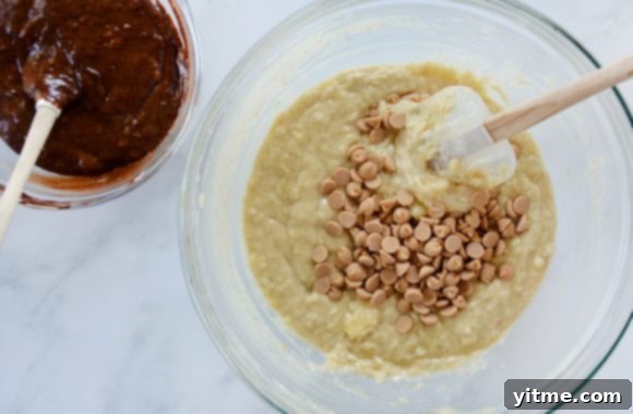 A small glass bowl containing chocolate banana bread batter with a spatula and a large glass bowl containing banana bread batter with peanut butter chips being stirred with a white spatula