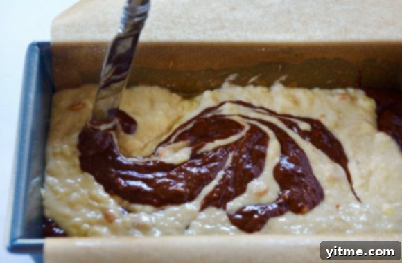 Knife swirling together banana bread batter and chocolate mixture in bread pan