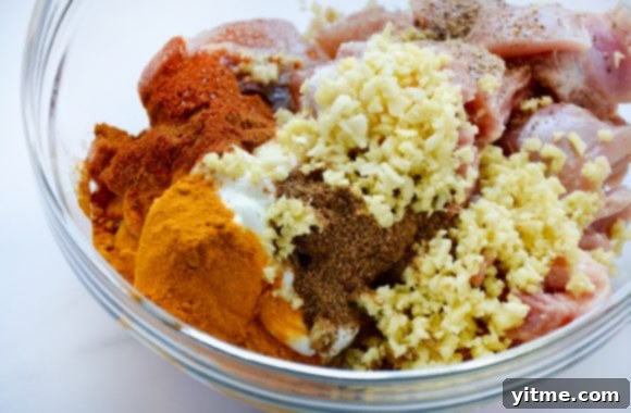 Irresistible Chicken Tikka Masala 3 A clear glass bowl showcasing the vibrant ingredients for a Chicken Tikka Masala marinade, including creamy yogurt, fresh grated ginger, minced garlic, and colorful spices like garam masala, turmeric, and paprika, ready to coat the chicken