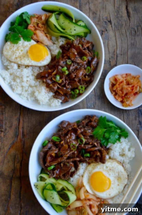 Top down view of two bowls containing easy beef bulgogi, white rice, a fried egg, cucumber ribbons, fresh cilantro and kimchi