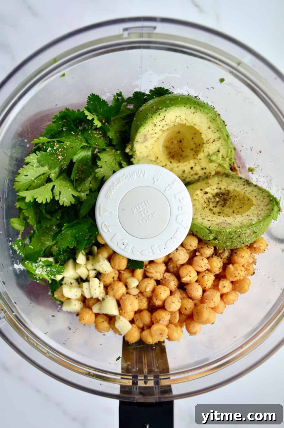 Chickpeas, chopped garlic, avocado halves, fresh herbs, salt, and pepper in a food processor