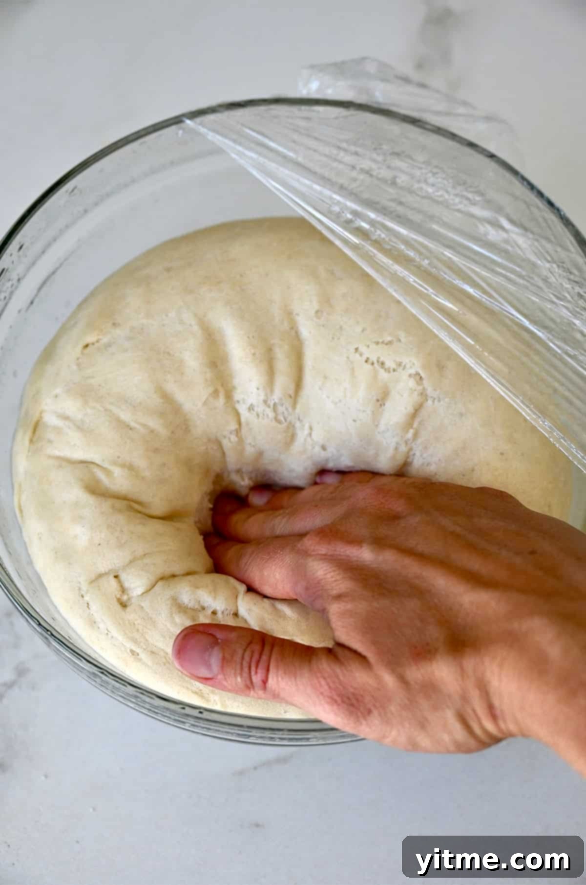 Punching down proofed dough in a bowl.