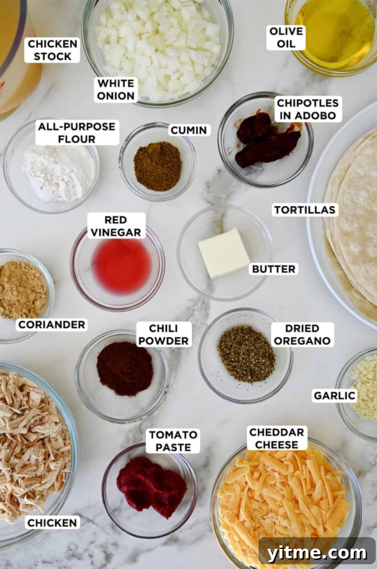 Weeknight Rotisserie Chicken Enchiladas 3 Various sizes of glass bowls containing ingredients to make rotisserie chicken enchiladas, including butter, flour, chicken stock, chipotles in adobo, tomato pasta, spices, red wine vinegar, onion, minced garlic, rotisserie chicken, shredded cheese and tortillas.