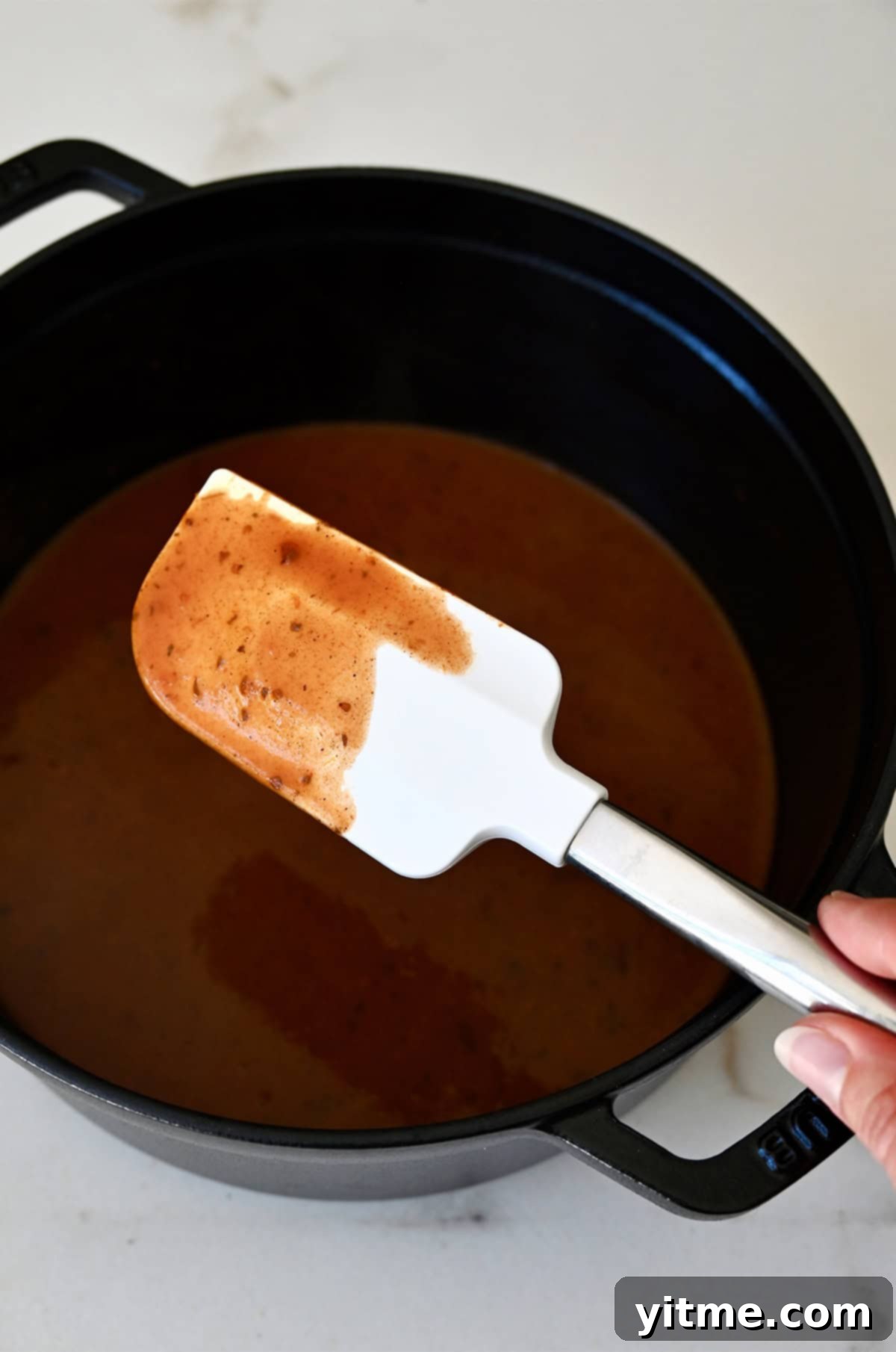 Weeknight Rotisserie Chicken Enchiladas 4 Homemade enchilada sauce covering a spatula above a sauté pan with more sauce.