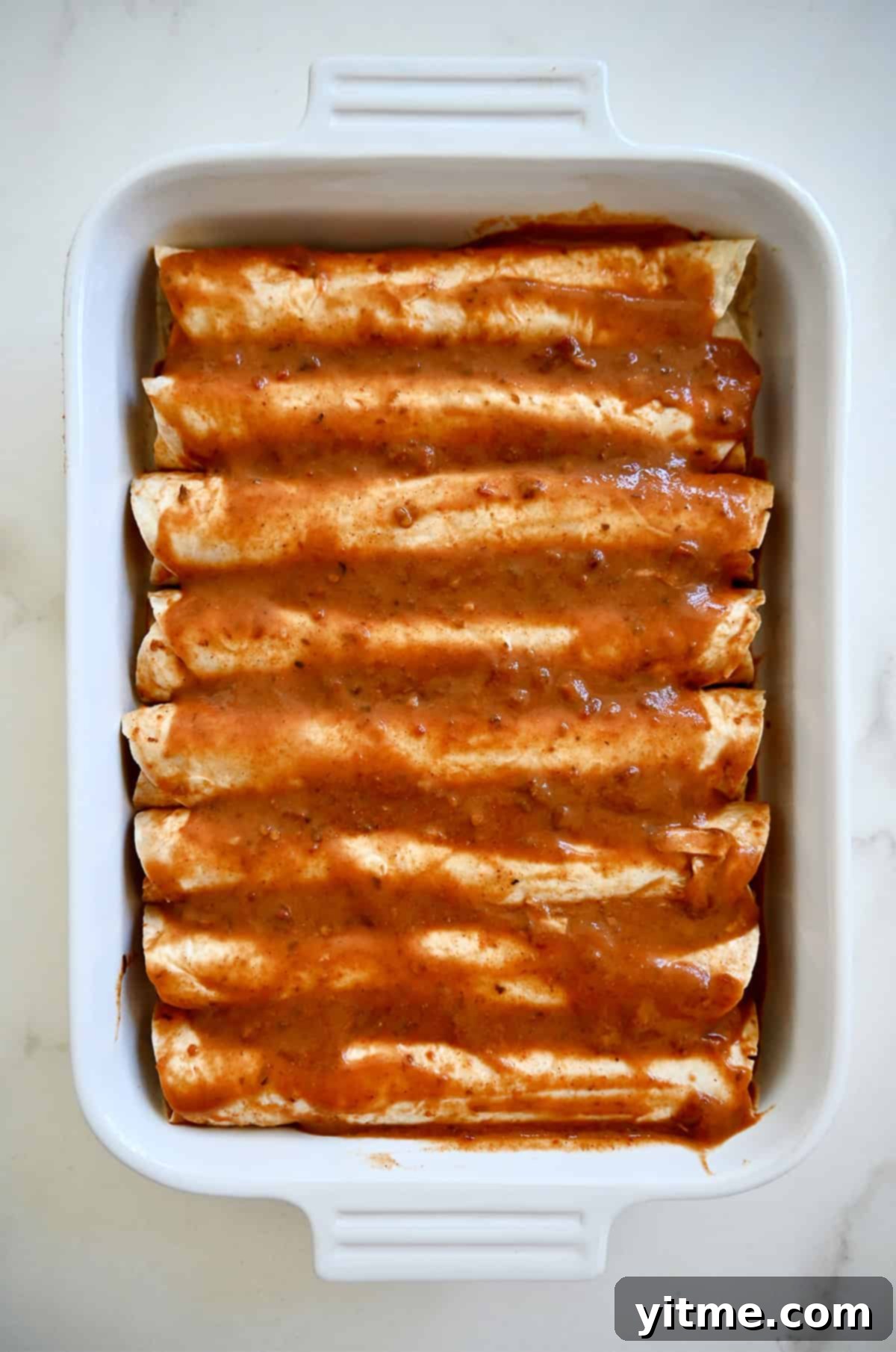 Weeknight Rotisserie Chicken Enchiladas 7 A single layer of enchiladas covered with homemade enchilada red sauce in a 9x13 baking dish.