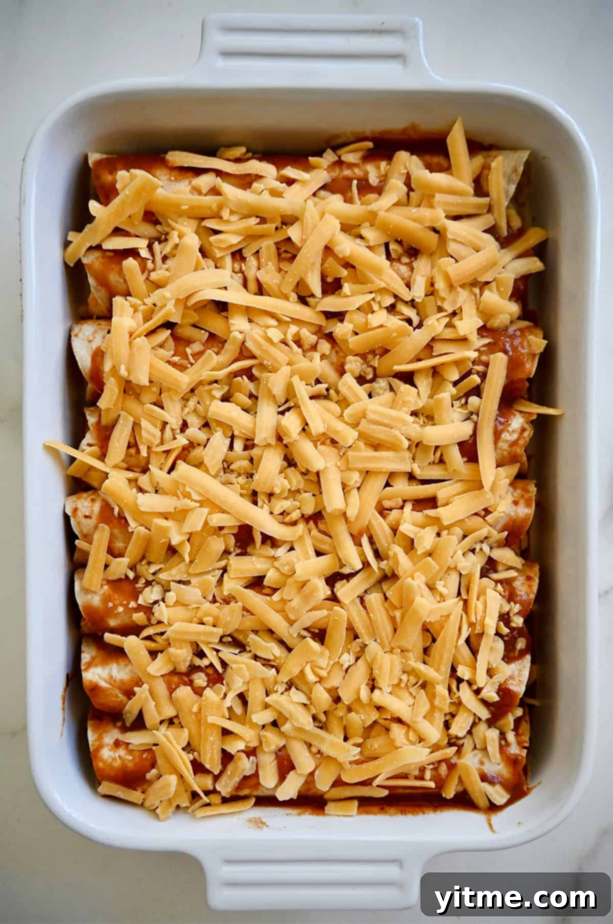 Weeknight Rotisserie Chicken Enchiladas 8 Shredded cheese atop unbaked enchiladas in a white baking dish.