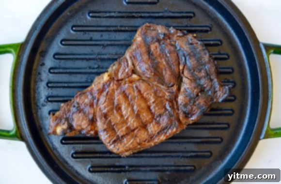 Seared ribeye steak sizzling on a grill pan, ready to be sliced and added to the salad.