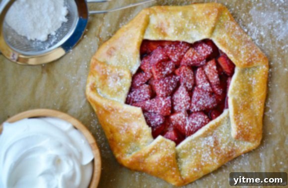 Strawberries and cream galette garnished with powered sugar next to bowl containing whipped cream
