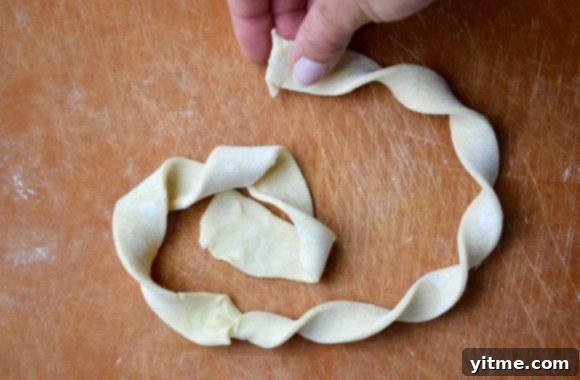 Puff pastry being twisted into a danish shape on a cutting board