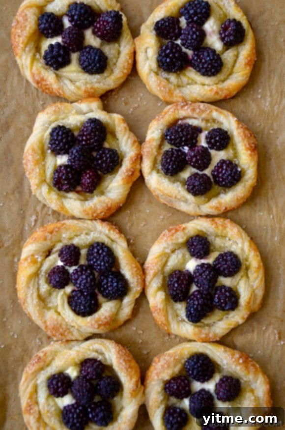 A baking sheet with brown parchment paper and blackberry pastries