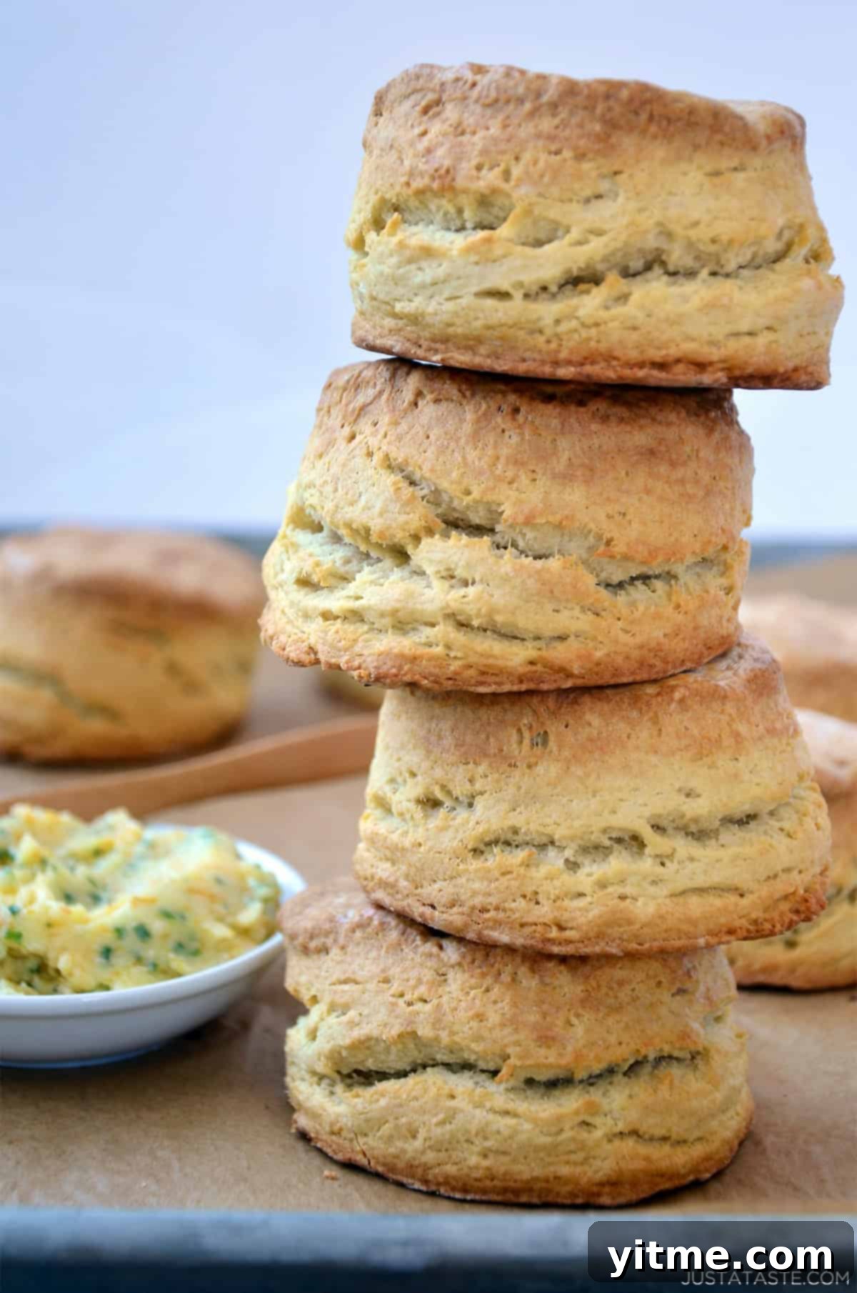 A tall stack of homemade buttermilk biscuits with a small bowl containing homemade honey butter nearby.