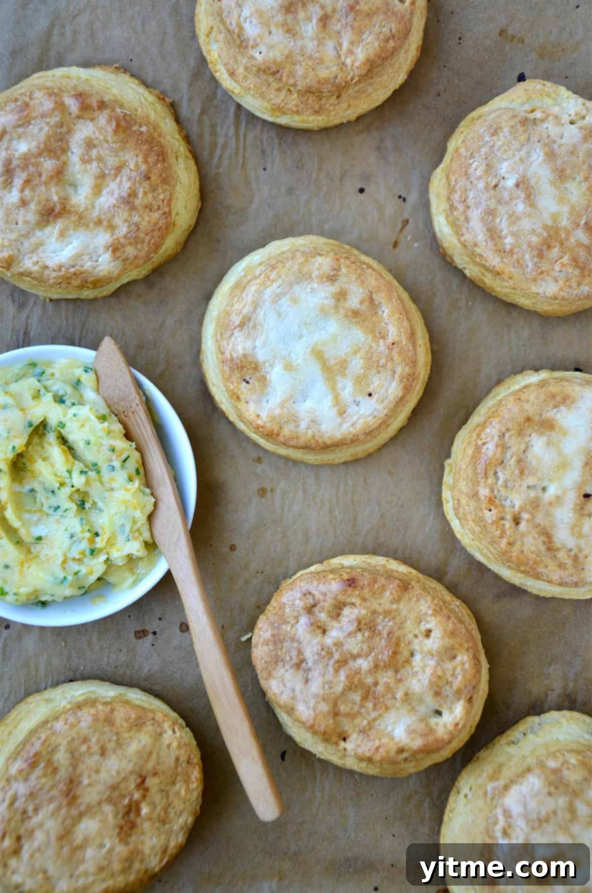 Buttermilk biscuits brushed with honey butter on a baking sheet with a small bowl containing honey butter.