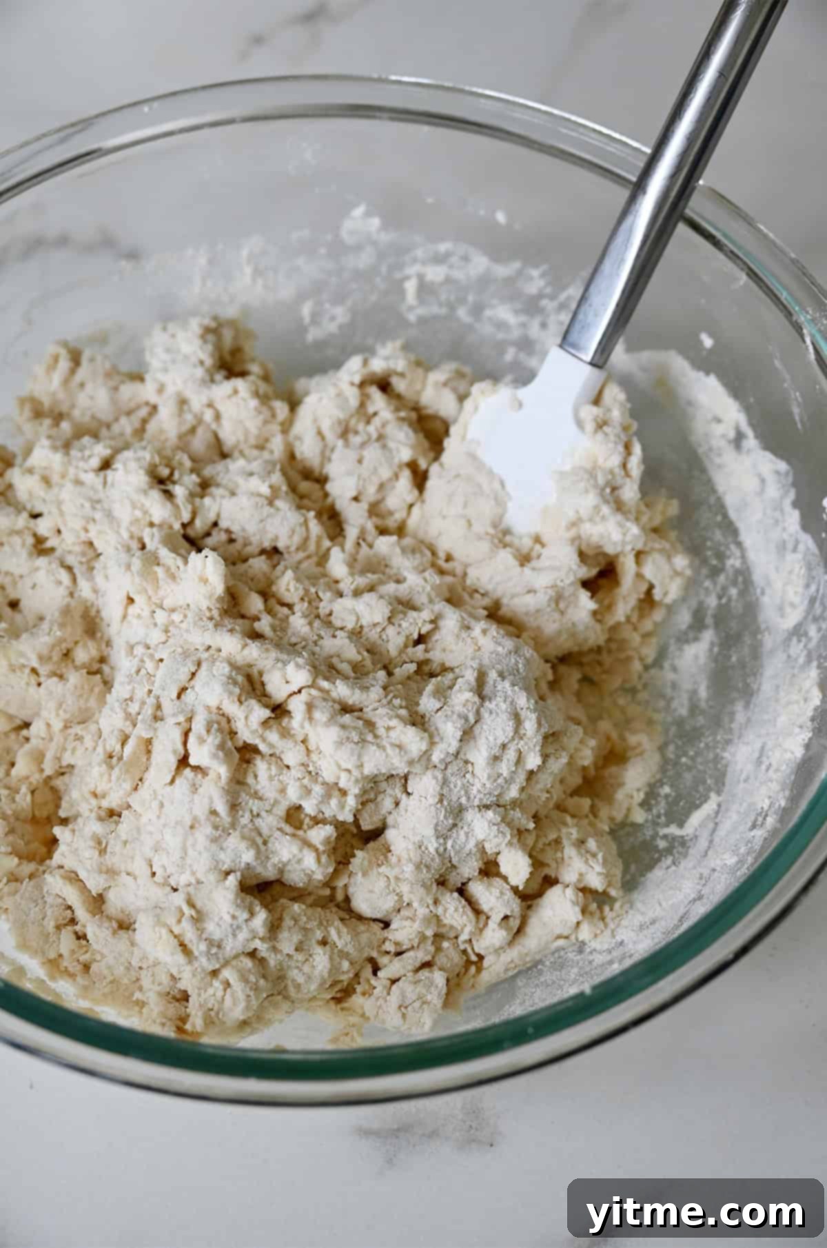 A shaggy buttermilk dough in a bowl with a spatula.