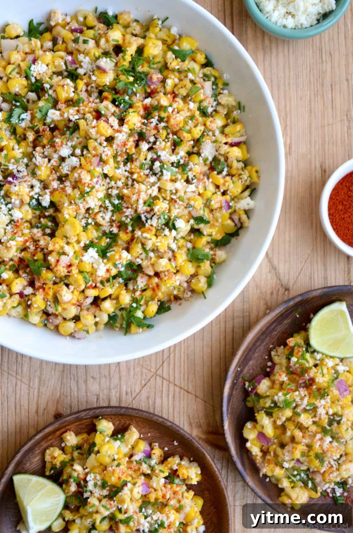 Elote Corn Salad in a large bowl with plates and lime